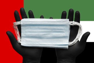 Doctor holds medical face mask in hands in black gloves on background colors national flag of