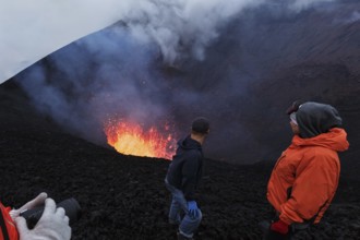Tourists watching the beautiful volcanic eruption, standing on the slope of dangerous cinder cone