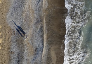 Aerial drone point of view of person walking on sand in a beach. Stormy waves idyllic beach in
