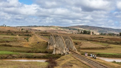 Malagasy people from the countryside cross a railroad bridge on the way to work and school on May