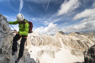 handsome male climber on a steep and exposed rock face climbs a Via Ferrata in Alta Badia in the