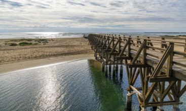 A long wooden boardwalk pier leads from one beach to another over a small ocean inlet