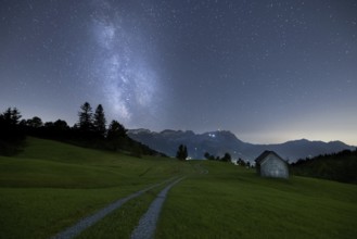 A clear night with a view of the Milky Way over a meadow and a remote hut with a mountain view,