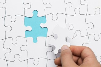 Human hand inserting white puzzle empty space