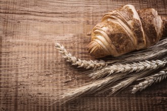 Yummy croissant bundle of wheat ears on oak wooden board food and drink concept