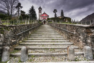long stairs leading up to an old rose colored church under an expressive overcast sky in the Maggia