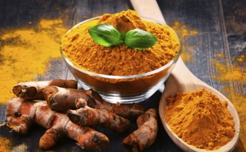 Composition with bowl of turmeric powder on wooden table