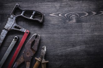 Rough vintage handsaw wire-cutter pliers on wooden board construction concept