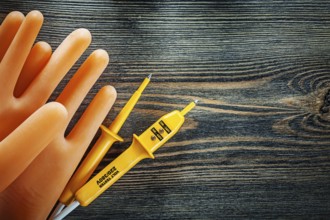 Pair of insulating gloves Electrical tester on wooden board