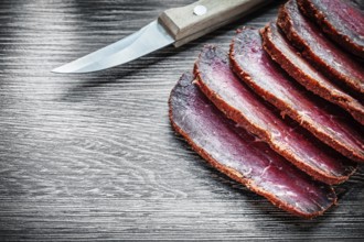 Smoked meat cut into slices, knife on wooden board