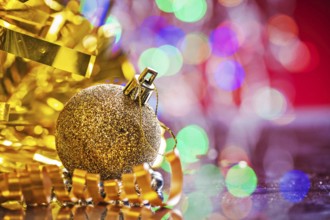 Gold colored christmas ball with tinsel and tape on mirror surface and blurred background