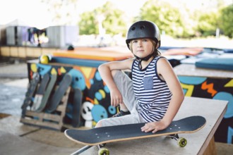 Boy sitting at skatepark, looking camera. Kid resting with skate board at skate park. child sits on