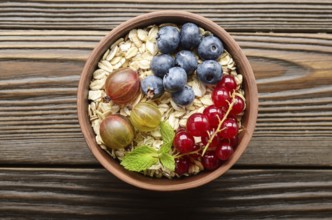 Flat lay view at oats in clay bowl with berries on wooden table