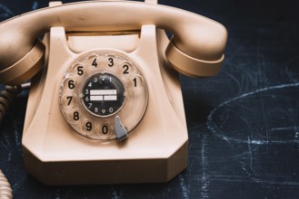Close-up of a beige vintage rotary phone on a dark surface, evoking a sense of nostalgia