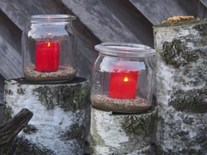 Red candles in glass jars on tree stumps against a rustic backdrop, borken, münsterland, germany