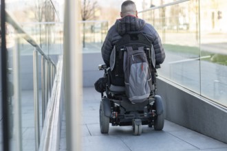 Man in a wheelchair using a ramp next to stairs