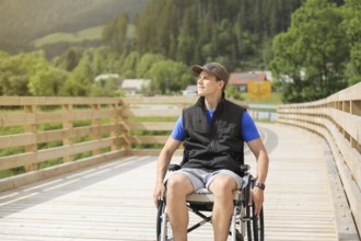 Disabled young man on a wheelchair on a wooden bridge path enjoying in nature looking at beautiful