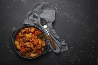 Beef meat stew with potatoes, carrot and delicious gravy in black casserole pot with bay leaves