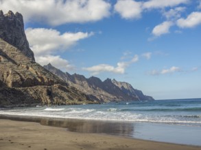 A picturesque beach with waves lapping against the sand and rocky cliffs and mountains in the