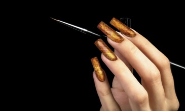 Hand with a beautiful golden manicure and a brush on a black background. Nail design. Extended