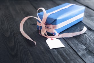 Classy blue gift, tied with pink ribbon and bow, with an empty label tied to it, on an old wooden