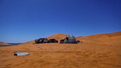 Camping scene in the desert under a starry night sky with tents and vehicles, tent camp in the