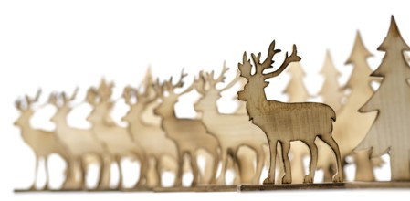 Deer figure sawn out of wood with dark edges and wooden fir trees cut out on white
