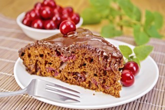 Chocolate cake with cherries on a plate, cherries, mint on a bamboo napkin on the background of