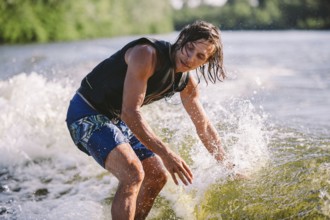 Active wakesurfer jumping on wake board down the river waves. Surfer on wave. Male athlete training