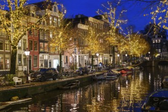 Festively decorated streets along a canal with lights and boats at night, Amsterdam, Netherlands