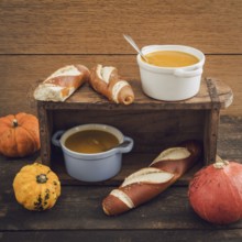 Homemade pumpkin soup in little cocotte cups and pretzel sticks on wooden table