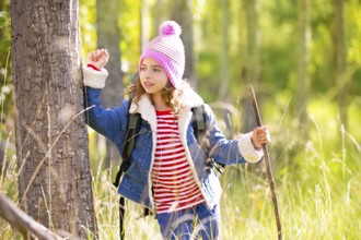 Hiking kid girl with backpack in autum poplar trees forest and walking stick