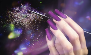 Hand with a beautiful manicure and a brush on a purple bokeh background. Nail design. Extended