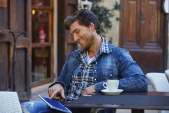 Young man with tablet pc touch in an cafe outdoor having some coffe cup