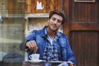 Young man with tablet pc touch in an cafe outdoor having some coffe cup