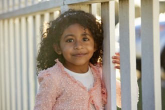 Happy toddler kid girl portrait in a park fence latin ethnicity