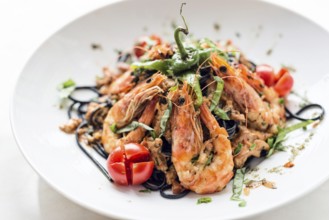 Gourmet food grilled prawn and vegetables on black squid ink pasta meal