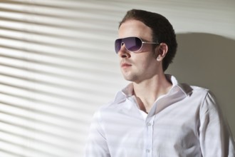 Man in sunglasses looks in the window, stripe shadows from the blinds, Belgium, Europe