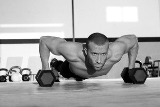 Gym man push-up strength pushup exercise with dumbbell in a crossfit workout