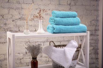 Rack with a stack of three colour turquoise towels and baskets with clean white towels and toilet