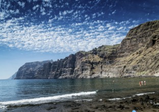 Tourists bathing at los gigantes volcanic black sand beach by famous natural cliffs landmark in