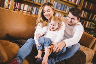 Christmas family portrait. Young Caucasian family in identical clothes having fun on sofa in living