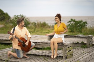 Woman dancing sitting on a beach while her boyfriend plays the guitar