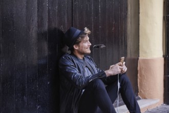 Young man with smartphone earphones sitting in the street black door