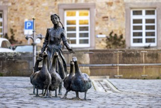 Statue of a girl with geese in front of a historic building, a parked car in the background, The