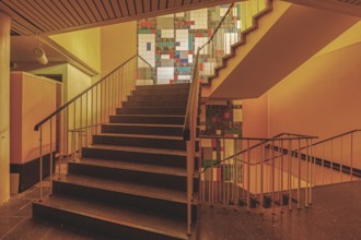 Interior with a staircase and railings, illuminated by yellowish light and with wall art, Bad am