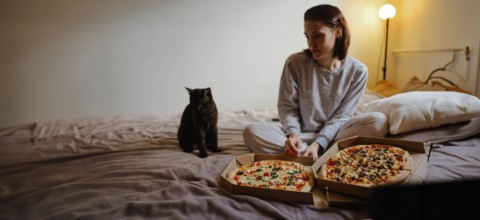 Woman and cat on bed with pizzas, soft lighting creating a cozy vibe