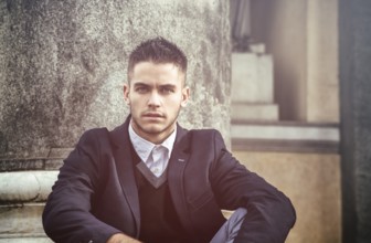 Handsome young man outdoor wearing jacket and shirt standing by historic building in European city.