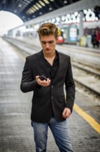 Attractive blond young man in train station using cellphone mobile