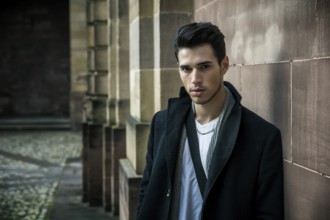 Handsome young man outdoor in winter fashion, wearing black coat and woolen scarf against historic